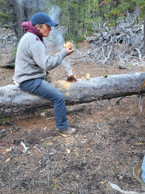 Person sitting on a log in a forest, holding a small object.